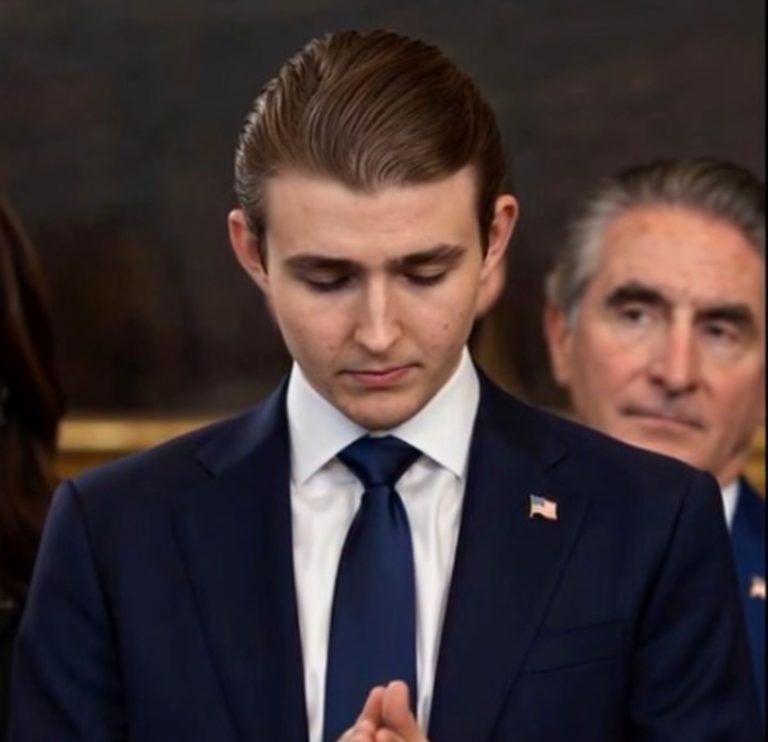 young man in navy suit with American flag pin stands with eyes closed and hands clasped