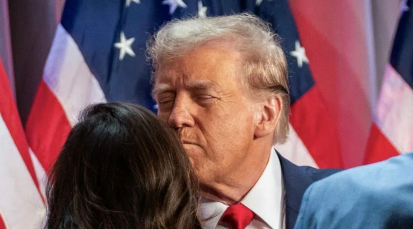 donald Trump closing eyes while embracing someone with American flags behind him