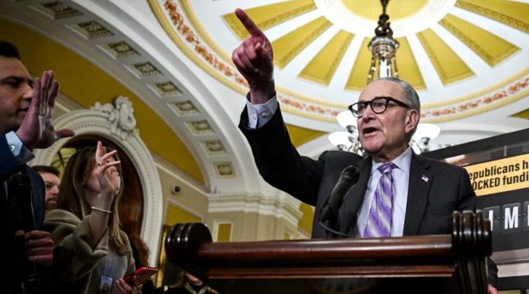 senator Chuck Schumer gestures emphatically at a podium beneath the ornate Capitol dome