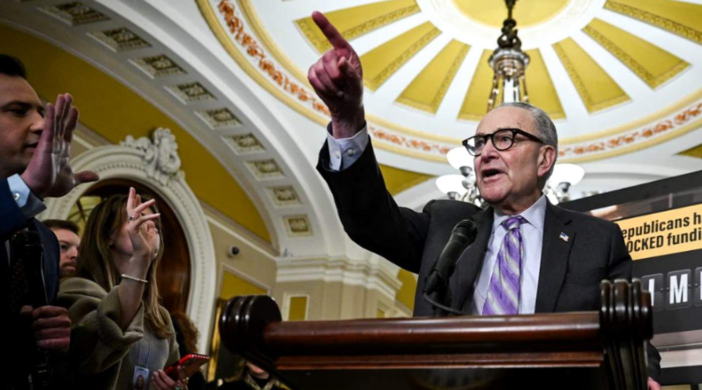 senator Chuck Schumer gestures emphatically at a podium beneath the ornate Capitol dome