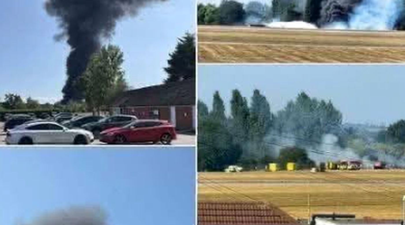 thick black smoke rising over fields and vehicles nearby