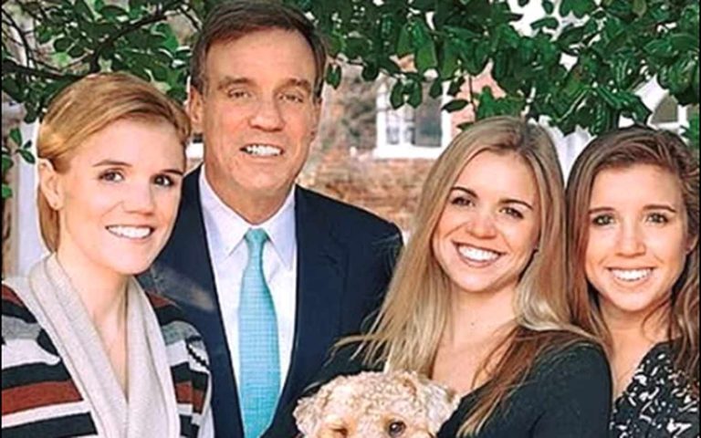 senator Mark Warner posing outdoors with three smiling young women and a small fluffy dog