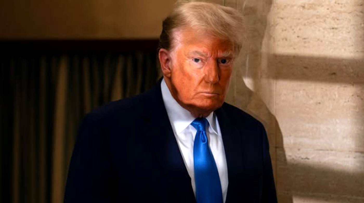 donald Trump in dark suit and bright blue tie standing beside marble column with serious