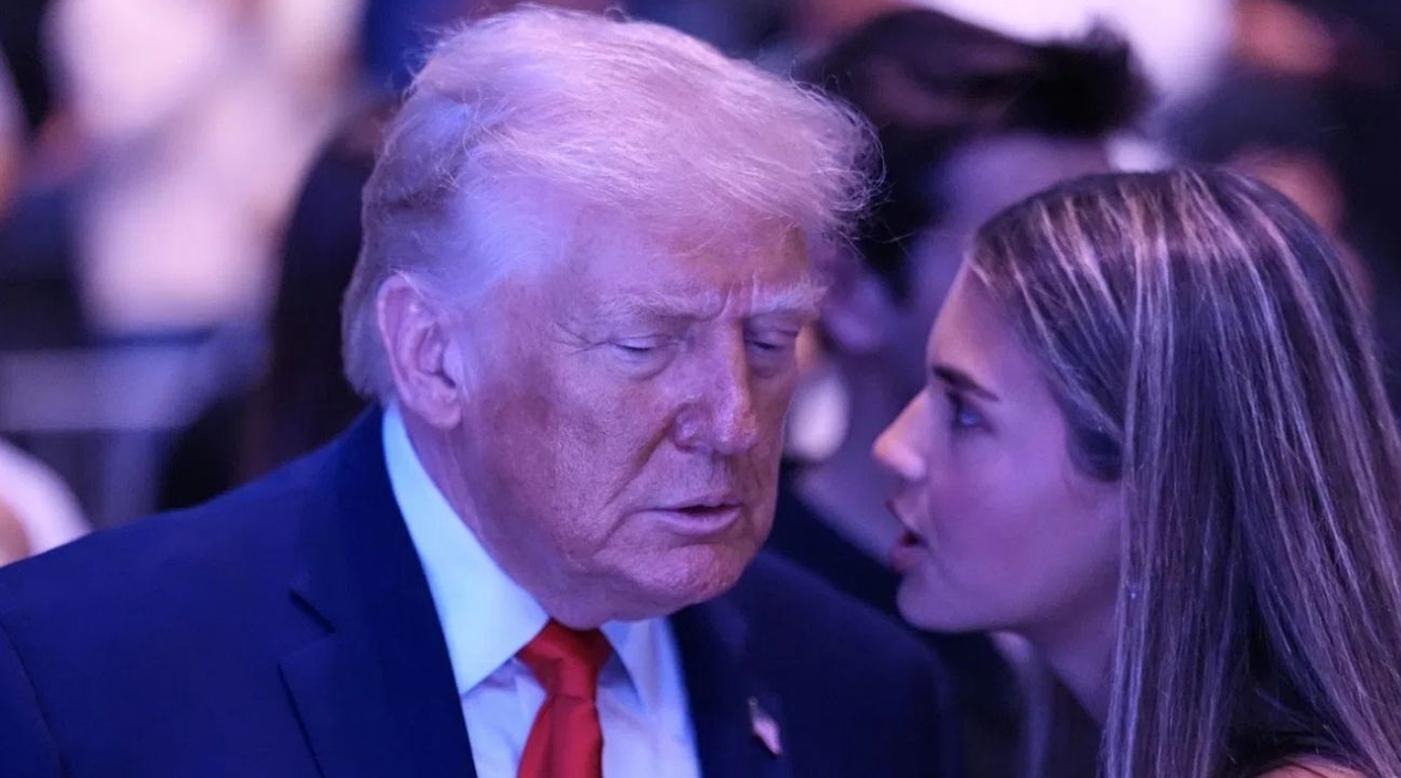donald Trump in navy suit and red tie listens intently to a woman with long brown hair at