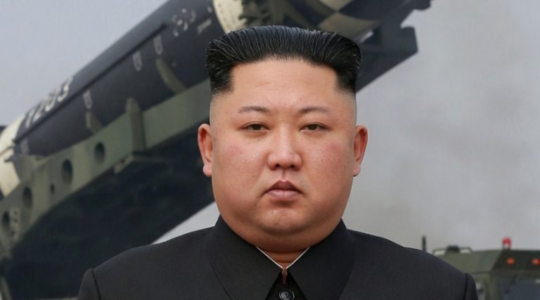 kim Jong Un in black suit with military vehicle and missile launcher in background