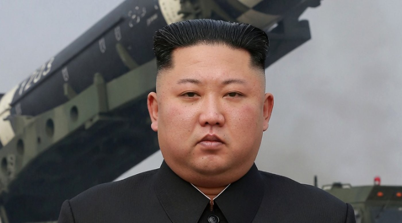 kim Jong Un in black suit with military vehicle and missile launcher in background