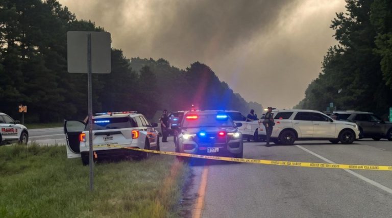 police cruisers with flashing lights block a rural highway behind yellow crime scene tape