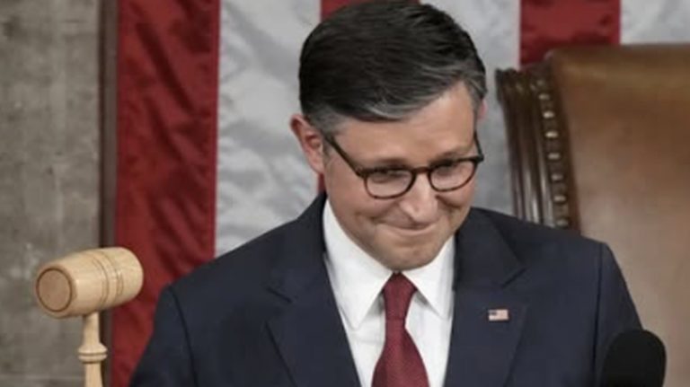 man in suit smiling with gavel and American flag backdrop