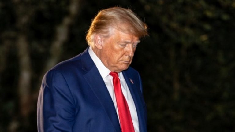 donald Trump looking down, wearing a suit and red tie at night