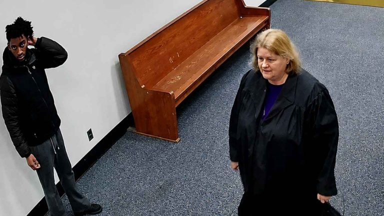 A judge in robes walking down a courtroom hallway.