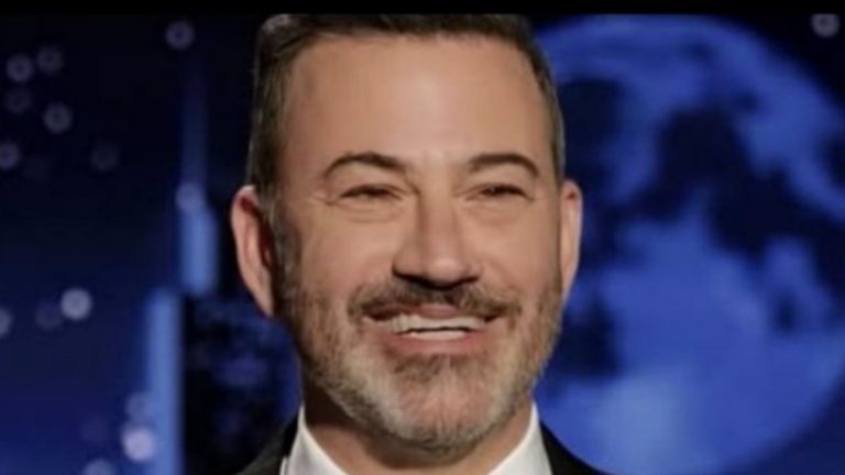jimmy Kimmel smiling on stage with a blue background