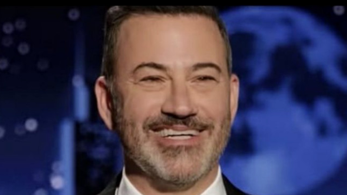 jimmy Kimmel smiling on stage with a blue background