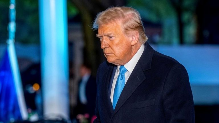 Donald Trump walking outside at night in a dark coat.
