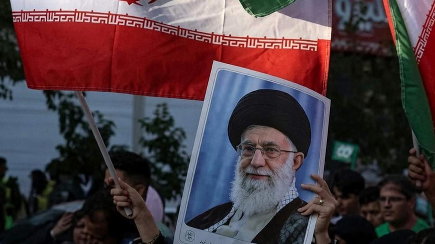 Protester holds poster of Khamenei and Iranian flag.