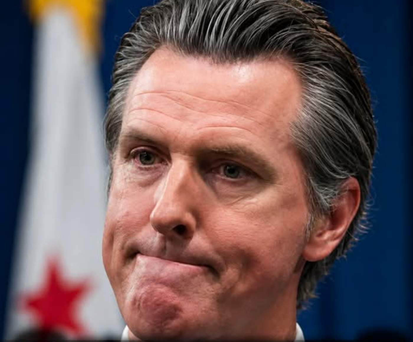 Gavin Newsom behind a breaking news banner.
